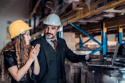 Engineer woman and businessman wearing a hardhat standing cargo at goods warehouse and check for control loading from Cargo freight ship for import and export by report on laptop. Teamwork concept © totojang1977