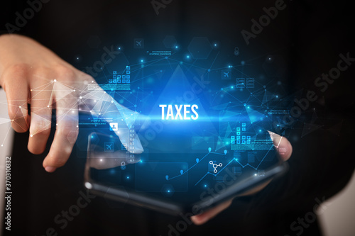 Businessman holding a foldable smartphone with TAXES inscription, business concept