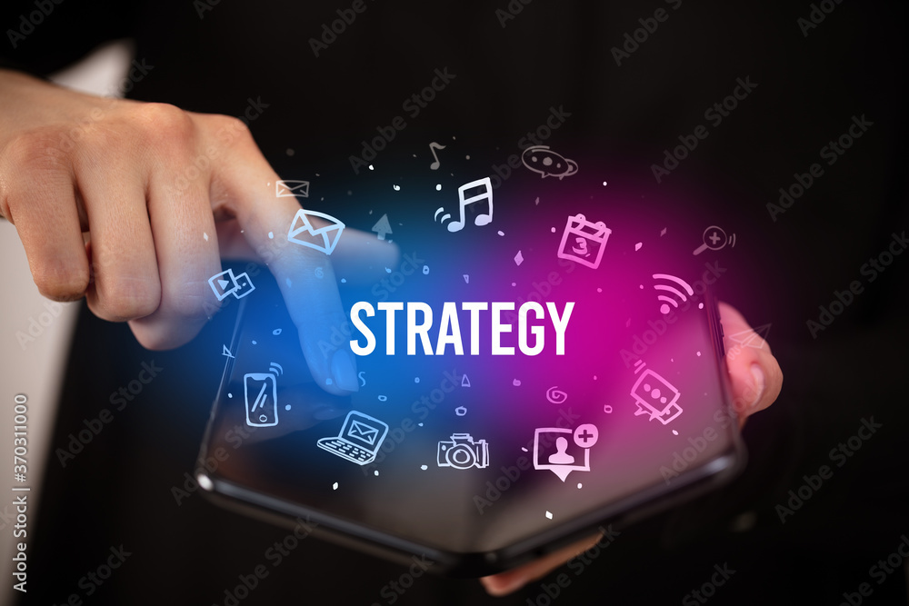 Businessman holding a foldable smartphone with STRATEGY inscription, social media concept Businessman holding a foldable smartphone with STRATEGY inscription, social media concept
