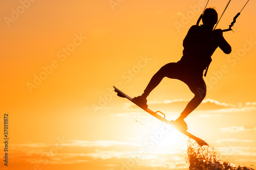 Silhouette of kitesurfer jumping in beautiful yellow sunset conditions with the sun right below his board
