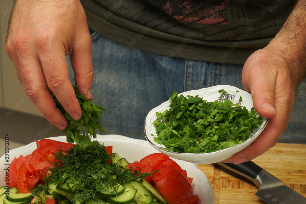 A man sprinkles dill and parsley on a freshly made cucumber and tomato salad. A man sprinkles dill and parsley on a freshly made cucumber and tomato salad.