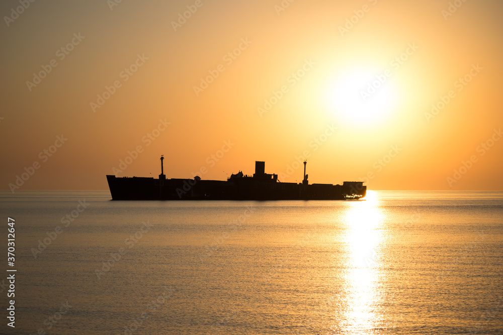 Beautiful landscape by the sea, at sunrise. The silhouette of a shipwreck. Golden colors