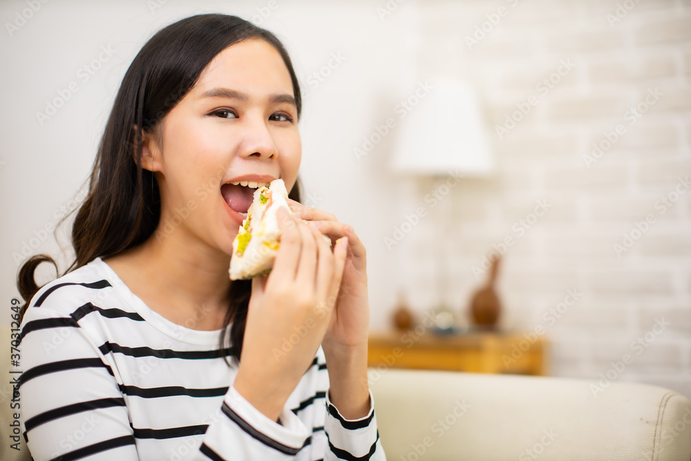 Young asian woman and happy eating healthy salad sitting on the table with green fresh ingredients indoors.greens in bowl for breakfast or lunch. she eating sandwich for breakfast. Young asian woman and happy eating healthy salad sitting on the table with green fresh ingredients indoors.greens in bowl for breakfast or lunch. she eating sandwich for breakfast.