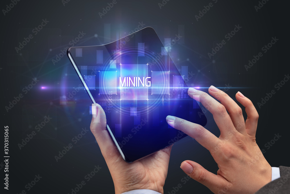 Businessman holding a foldable smartphone with MINING inscription, new technology concept Businessman holding a foldable smartphone with MINING inscription, new technology concept