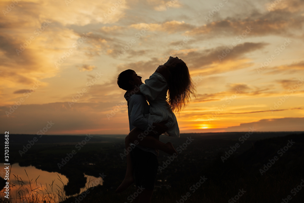 Silhouette of happy guy holding his passionate girlfriend at wonderful sunset. Man holding up his woman in his arms. Young couple in each other's arms on sunset. Copy space.