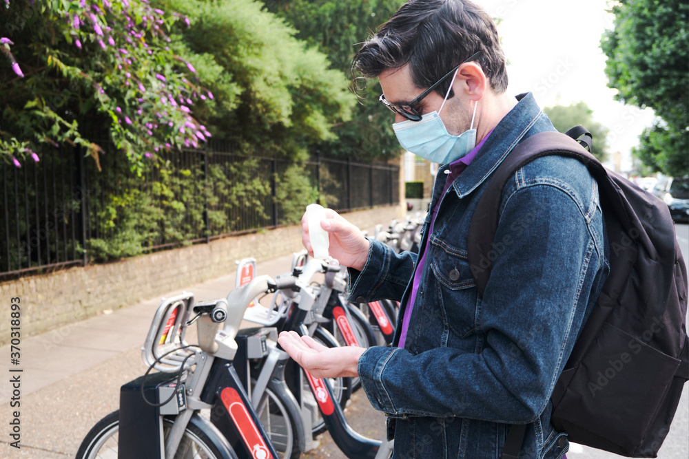 Man covering his face and using antibacterial hand sanitizer in front of rental electric bikes Man covering his face and using antibacterial hand sanitizer in front of rental electric bikes