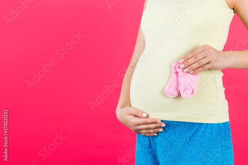 Wallpaper Mural Close up portrait of pregnant woman in colorful home clothing holding pink socks for a baby girl at pink background. Waiting for a child. Copy space Torontodigital.ca