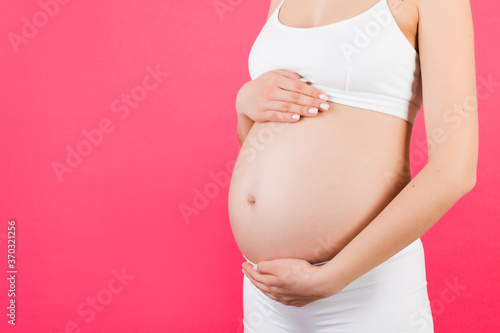 Close up of pregnant woman in white underwear holding her belly at pink background. Motherhood concept. Copy space © sosiukin