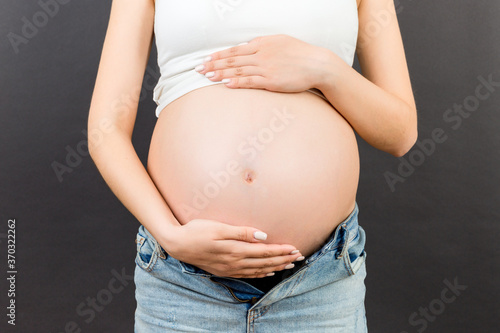 Cropped image of pregnant woman in unzipped jeans showing her naked belly at colorful background with copy space. Baby expecting concept