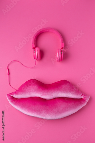 Giant mauve lips made of plush with pink headphones. Big juicy plush lips on a monochrome pink background. Pink headphones and women's lips made of plush in a mauve color. photo