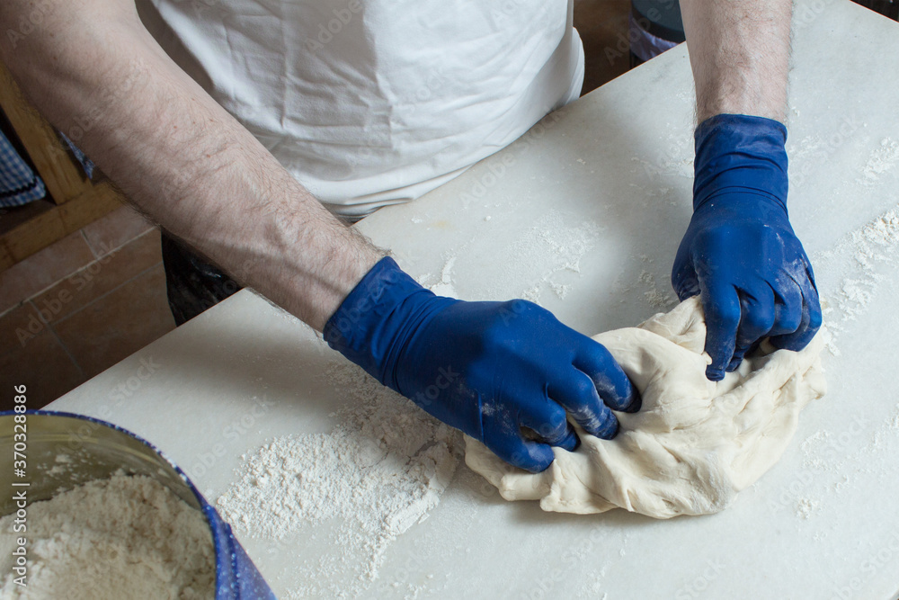 The baker shapes the dough with his hands covered with blue gloves. Steps to make bread at home.