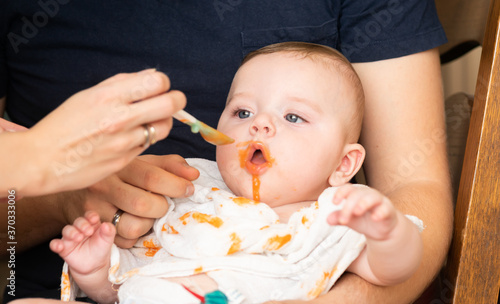 Obraz na płótnie Tiny baby boy eating his vegetable carrot meal for the first time. Parents feeding a baby with a spoon - expanding diet. w salonie