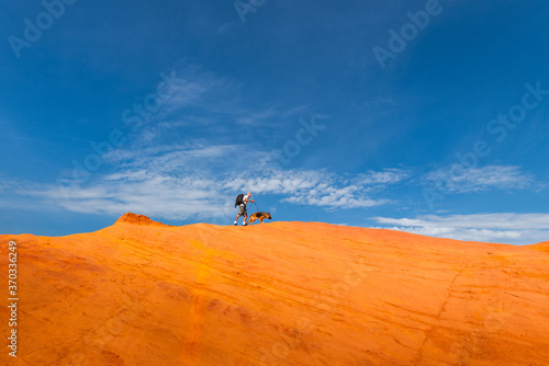 Man Walking with Dog on Edge of Red Mountains at Blue Sky