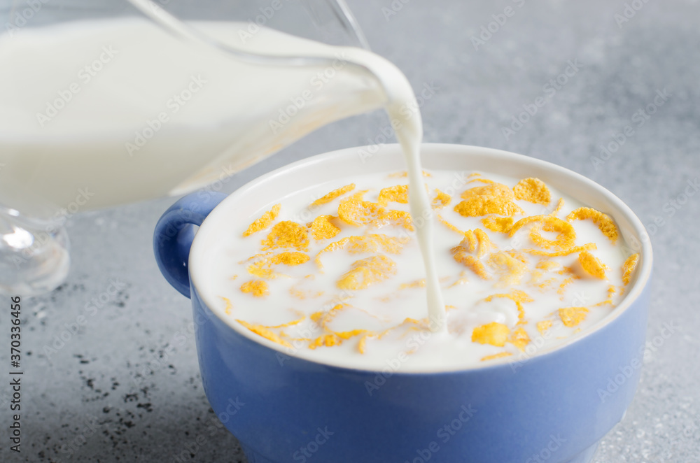 Milk is poured into corn flakes. Blue Cup on a concrete background. Healthy and nutritious Breakfast Milk is poured into corn flakes. Blue Cup on a concrete background. Healthy and nutritious Breakfast