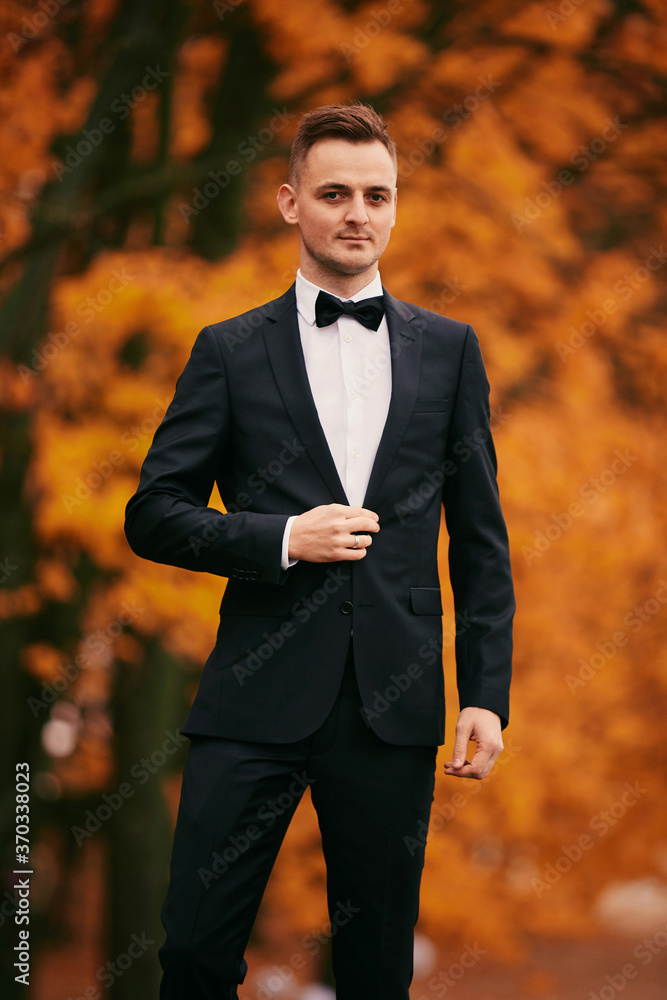 stylish young groom in a black suit in the autumn park on wedding day stylish young groom in a black suit in the autumn park on wedding day