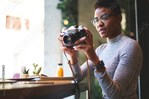 Attractive afro american photographer making pictures of cafe interior earning money using creative ideas,young casually dressed female black model pending time on hobby taking photo on vintage camera photo