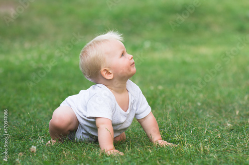 Little baby is crawling on all fours in the garden, baby crawling on green grass and looking up, banner copy space