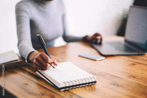 Selective focus on handwriting in notepad with blank pages during creative working process, cropped image of blurred afro american businesswoman copying information from web site using laptop
