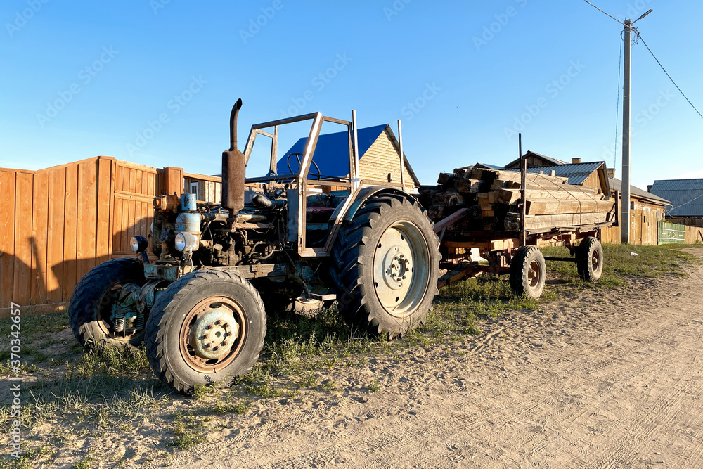 Old rusty abandoned agricultural tractor in a grass field tractor with trailer