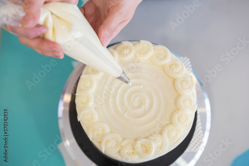 Woman pastry chef decorating cream and cheese cake in bakery shop.Decorating cake with a pastry bag with cream.Top view.Celebrations food concept