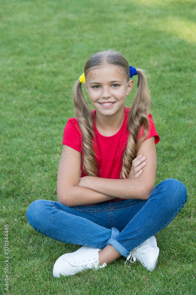 Little girl cute ponytails hairstyle relaxing on green grass, child care concept Little girl cute ponytails hairstyle relaxing on green grass, child care concept