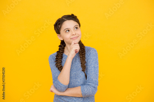 thoughtful girl with braids. adorable daydreaming kid. think about future. Portrait of pensive teen girl on yellow background. Let me think. Doubt concept. Doubtful child remembering something photo