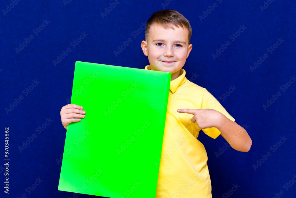 Happy calm caucasian child boy holding a poster for your information on the blue background Happy calm caucasian child boy holding a poster for your information on the blue background
