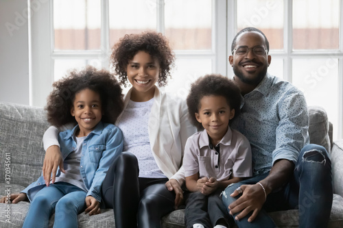 Portrait of smiling young african American family with two kids sit on couch at home relaxing on weekend, happy biracial parents rest on sofa with small ethnic children, enjoy leisure time together © fizkes