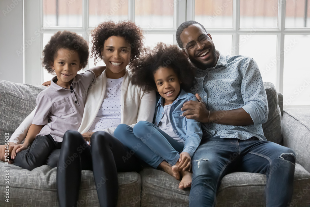 Portrait of smiling young african American family with two little children sit relax on couch at home, happy biracial parents rest on sofa in living room with small kids, enjoy weekend together Portrait of smiling young african American family with two little children sit relax on couch at home, happy biracial parents rest on sofa in living room with small kids, enjoy weekend together