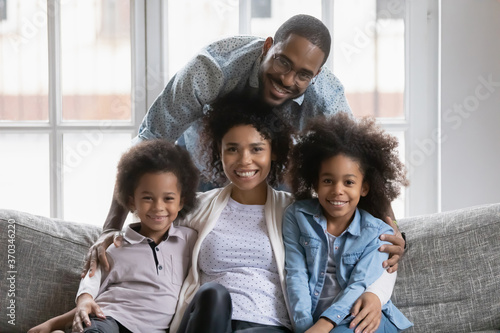 Portrait of happy african American young family with little kids son and daughter relax on couch at home hugging, smiling biracial parents enjoy weekend with small children, rest on sofa together © fizkes