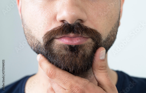 Foto Close up of young bearded man touching his beard while standing against gray bac