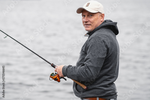 A fisherman in a baseball cap with a fishing rod in his hands smiles. Concept of healthy outdoor recreation.