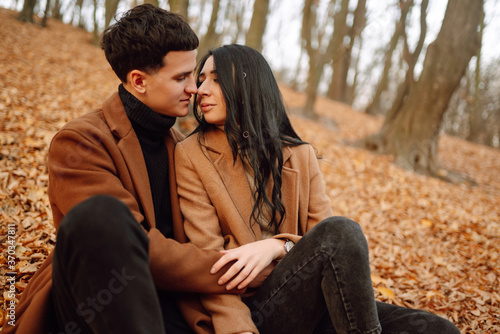 Young couple in love walking in the park on a autumn day. Enjoying time together. Stylish and loving couple enjoying each other in the autumn forest. 