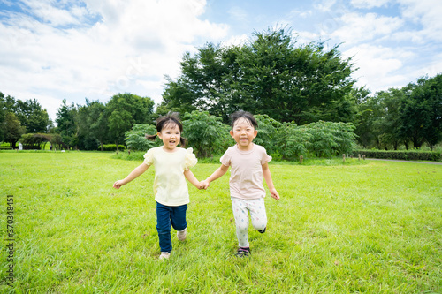 青空の下、公園の草原を元気に走る子供たち