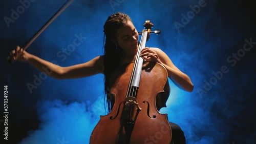 Young beautiful woman playing a melody on cello. Smoky dark studio