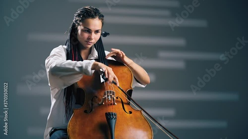 Young beautiful woman playing on cello in the spotlight. Grey background