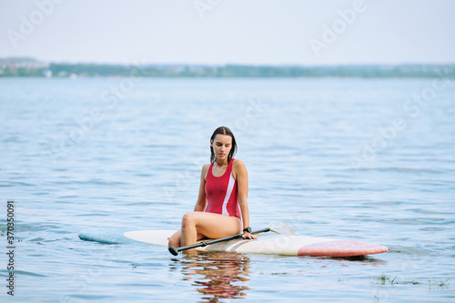 Relaxed woman in swimsuit sitting on surfboard with paddle and floating on water