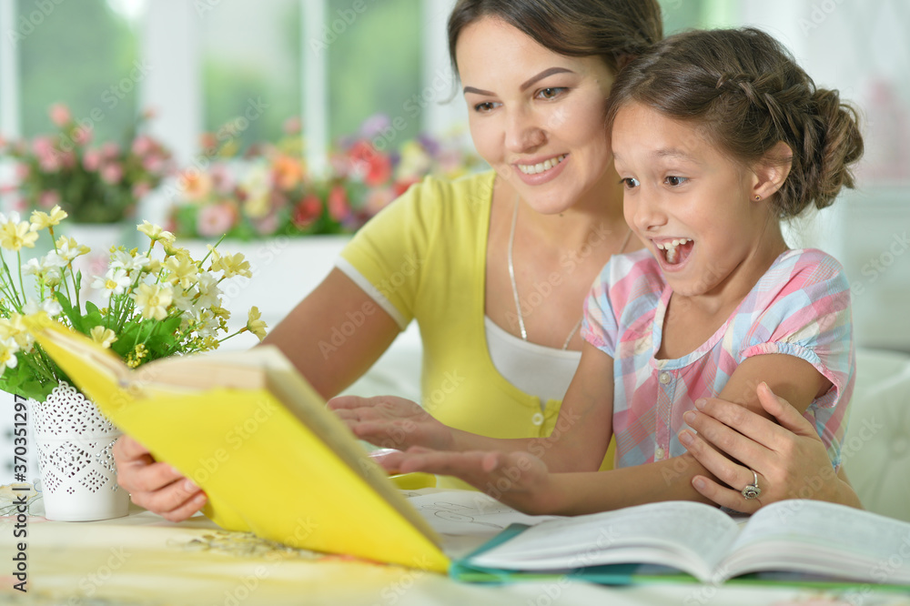 Little cute girl reading book with mother at the table at home Little cute girl reading book with mother at the table at home
