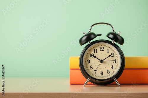 Stack of books and alarm clock on wooden table