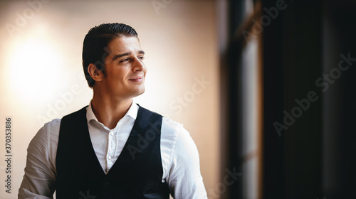 Portrait of a Smiling Caucasian Businessman, Standing by the Window and Looking outside