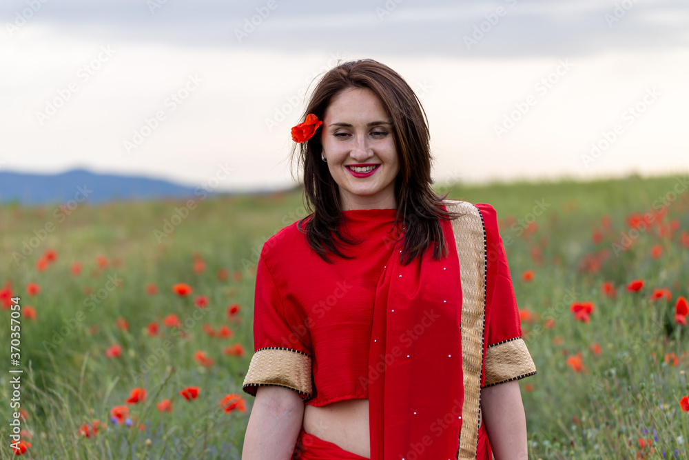 Yound girl dressed in Indian Sari in a poppy flower garden Yound girl dressed in Indian Sari in a poppy flower garden