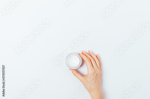 Small jar of cosmetic face cream in female hand