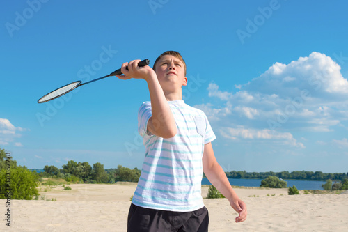 Boy playing badminton outdoors on the beach on a summer sunny day. Healthy lifestyle.