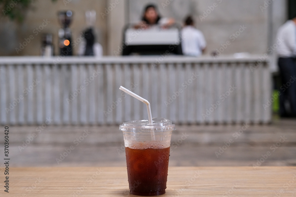 Iced black coffee in a clear plastic mug placed on a wooden table in the coffee cafe. Iced black coffee in a clear plastic mug placed on a wooden table in the coffee cafe.