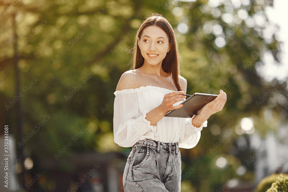 Portrait of beautiful brunette. Model in summer city. Girl standing with a tablet.
