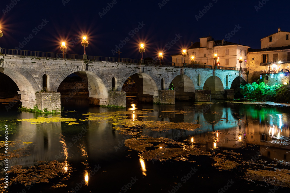 Vue nocturne sur le Pont Tibère et sa réflexion sur les eaux du fleuve Vidourle à Sommières (Occitanie, France)