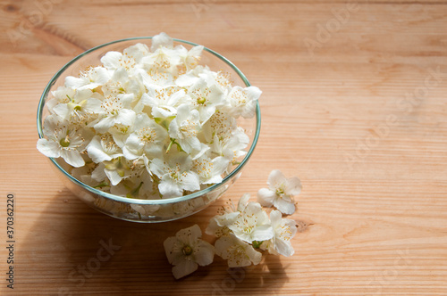 White jasmine flowers in a glass bowl on a wooden background. Collecting herbs and flowers for tea or home cosmetics. Harvesting of jasmine.