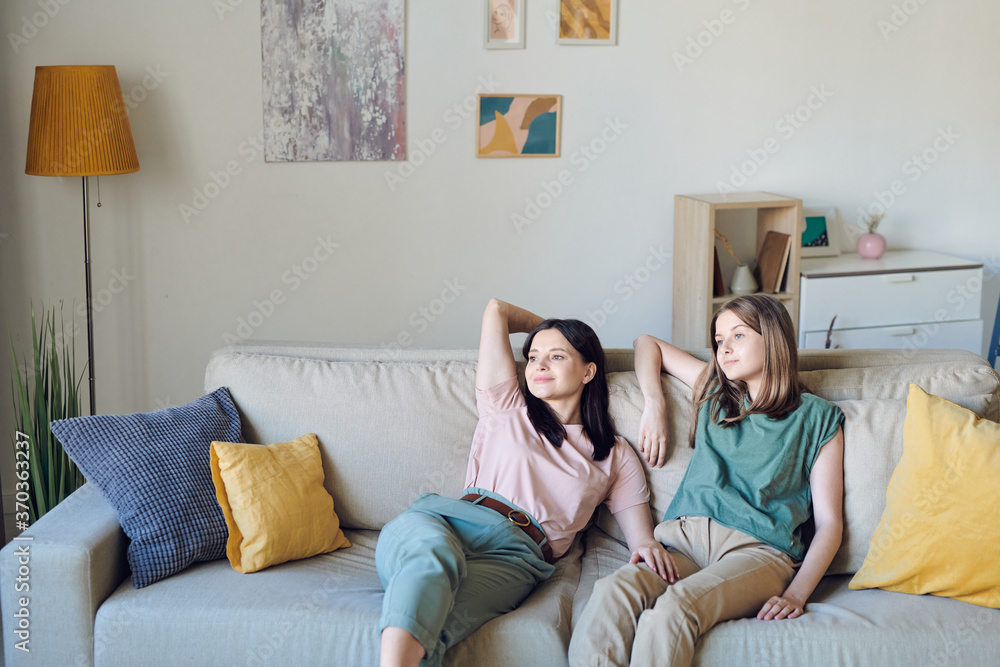 Young mother and daughter relaxing on couch in living-room against wall Young mother and daughter relaxing on couch in living-room against wall