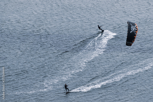 Two men kite surfing in different directions, one of them using a pirate themed kite