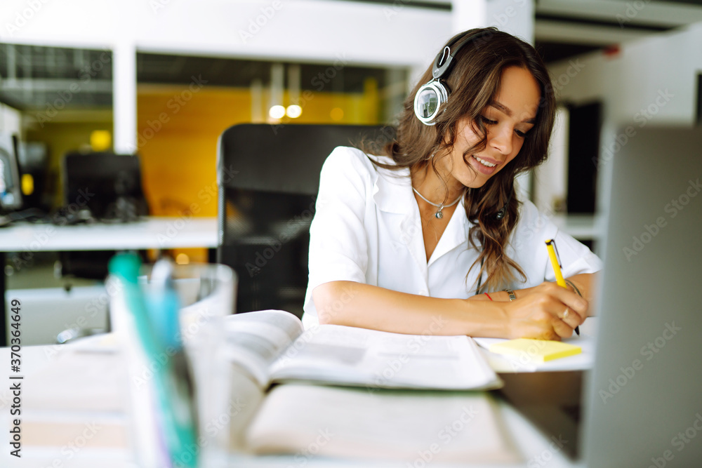 Young woman student wear wireless headphone study online. She learn language listen lecture watch webinar write notes look at laptop, distant education. Video call self-isolation during ncov situation